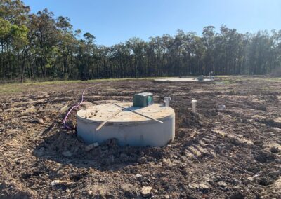 Concrete septic tanks installed in a cleared, muddy field with surrounding forest. - Fosker Plumbing Western Sydney