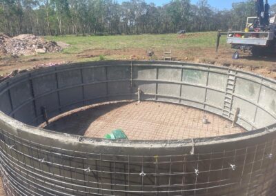 Large circular concrete tank under construction with metal reinforcements on grassy site. - Fosker Plumbing Western Sydney