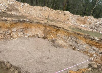 Excavated construction site with leveled gravel base and surrounding caution tape in wooded area. - Fosker Plumbing Western Sydney