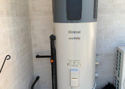 Tall Rinnai Enviroflo hot water storage unit installed against a brick wall in a corner. - Fosker Plumbing Western Sydney
