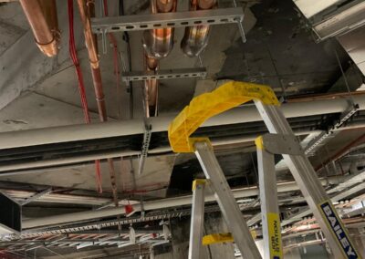 Exposed copper plumbing pipes on ceiling above a metal ladder in construction site.